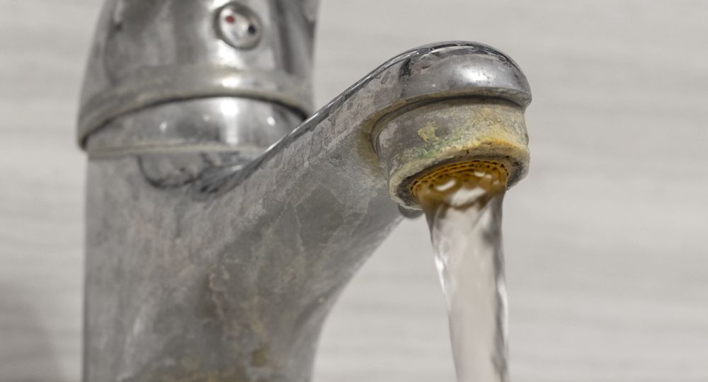 Old Bathroom Sink Faucet contaminated with calcium and grime. Hard water flows from an old tap aerator.